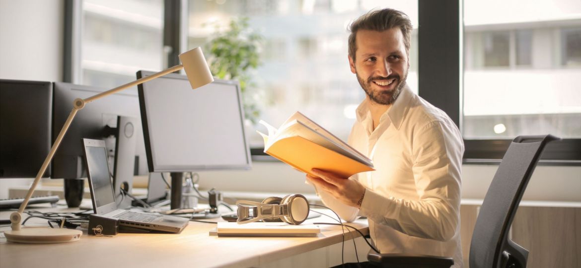 man sitting at desk with a book in his hand