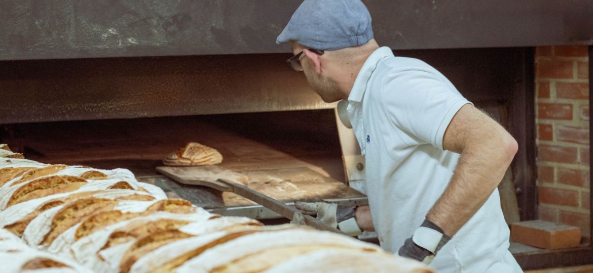 man scooping bread out of brick oven